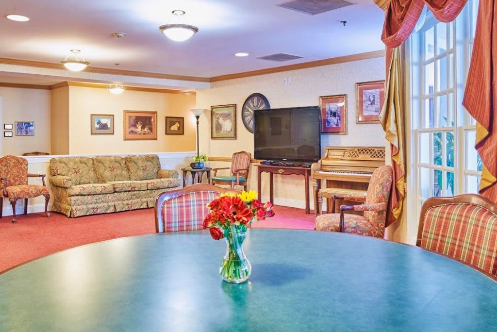 A cozy living room featuring a sofa, television, piano, and a table with flowers.