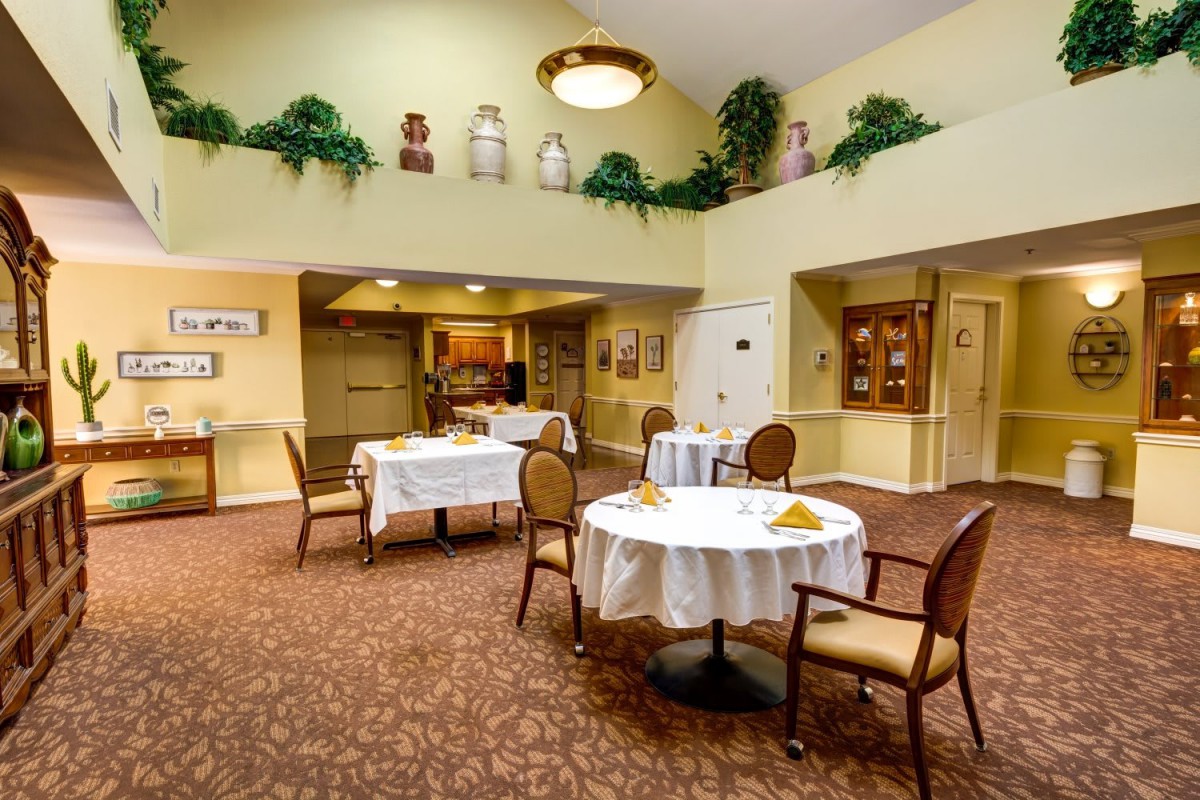 A cozy dining area with neatly arranged tables and chairs, featuring warm decor and potted plants.