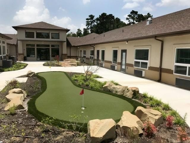 An outdoor mini-golf course next to a building, surrounded by landscaping and greenery.