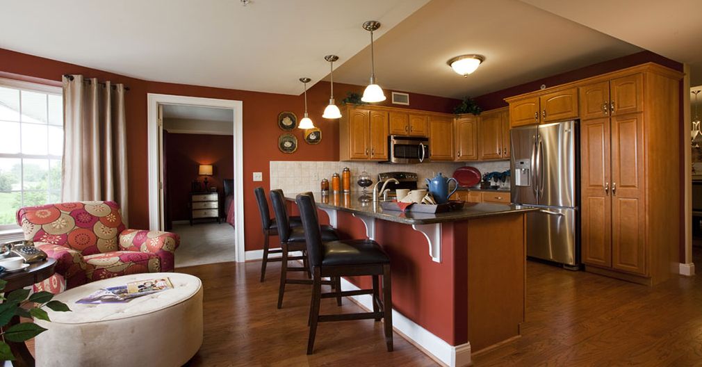 A modern kitchen interior with wooden cabinets and a countertop, featuring bar stools and pendant lighting.