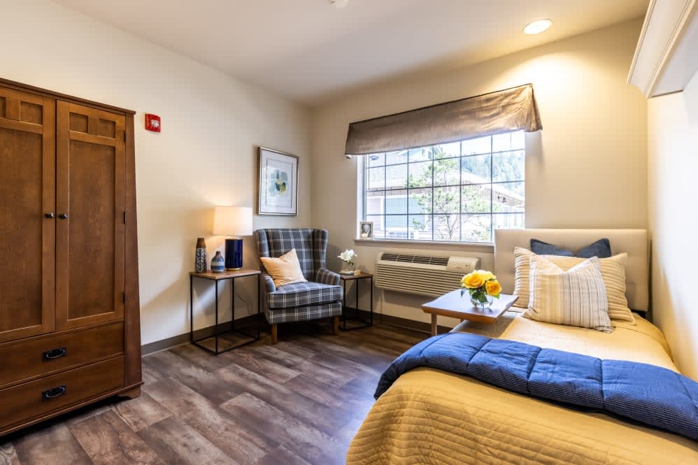A cozy bedroom featuring a comfortable bed, plaid armchair, and a window letting in natural light.