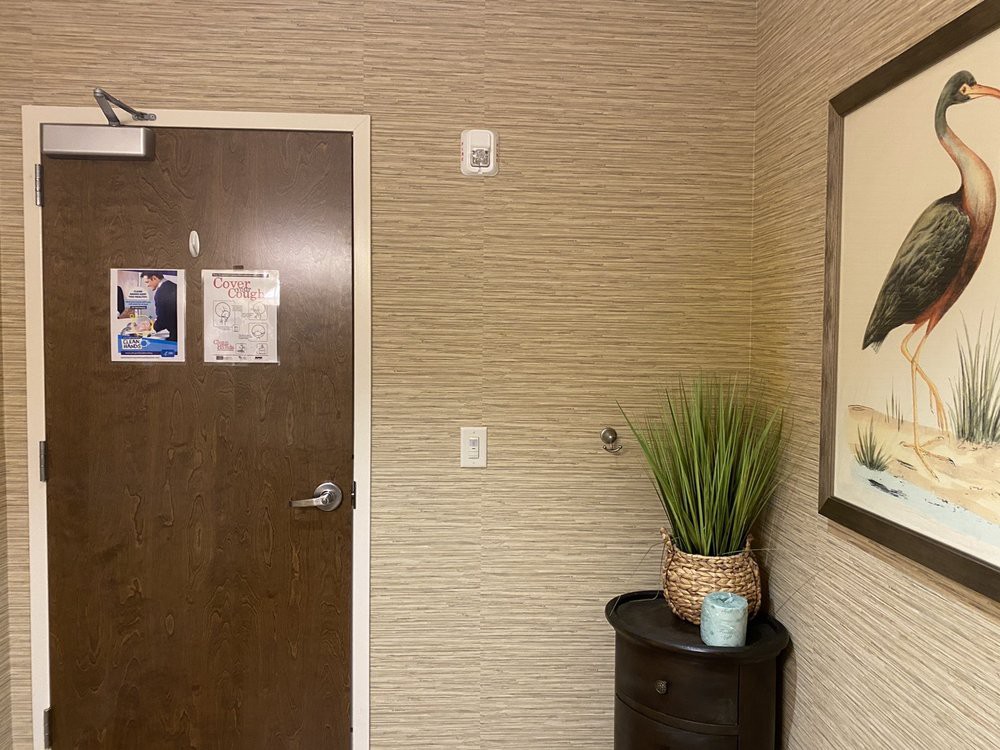 A hallway with a closed door, potted plant on a small table, and framed wall art.