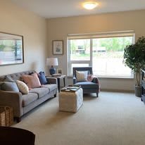 A cozy living room with a sofa, armchair, and coffee table beside a large window.