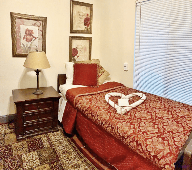 A cozy bedroom with a single bed adorned with red and beige bedding, decorative pillows, and wall art.