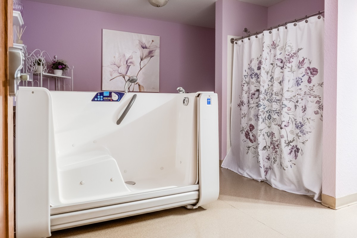 A modern bathroom featuring a walk-in tub with pink walls and a floral shower curtain.