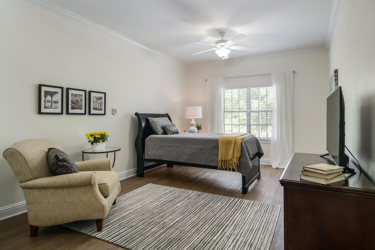 A modern and cozy bedroom with a neatly made bed, an armchair, and a large window allowing natural light to flood in.