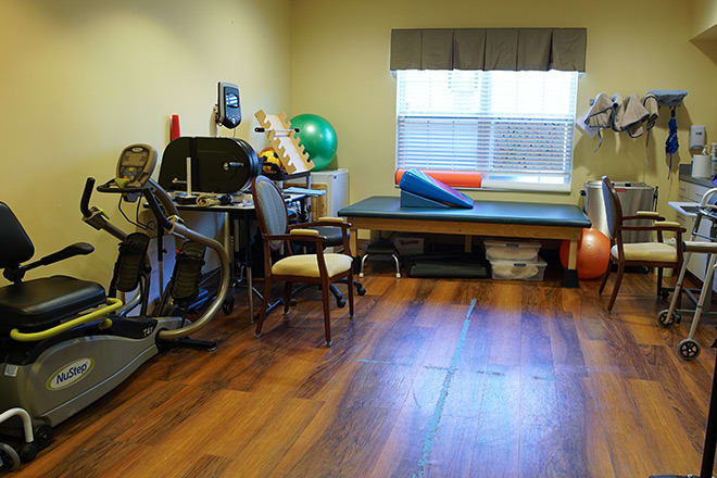 A physical therapy and exercise room equipped with various fitness tools, including a stationary bike and exercise ball.