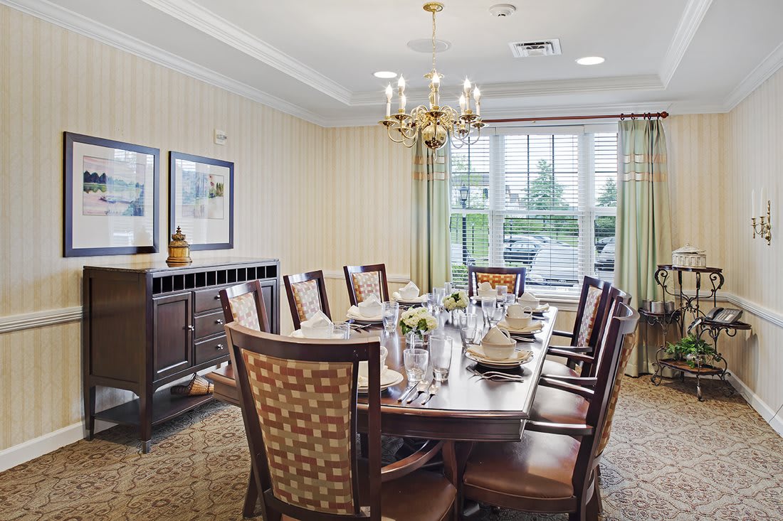 An elegant dining room with a long table set for a meal, featuring a chandelier and large windows.