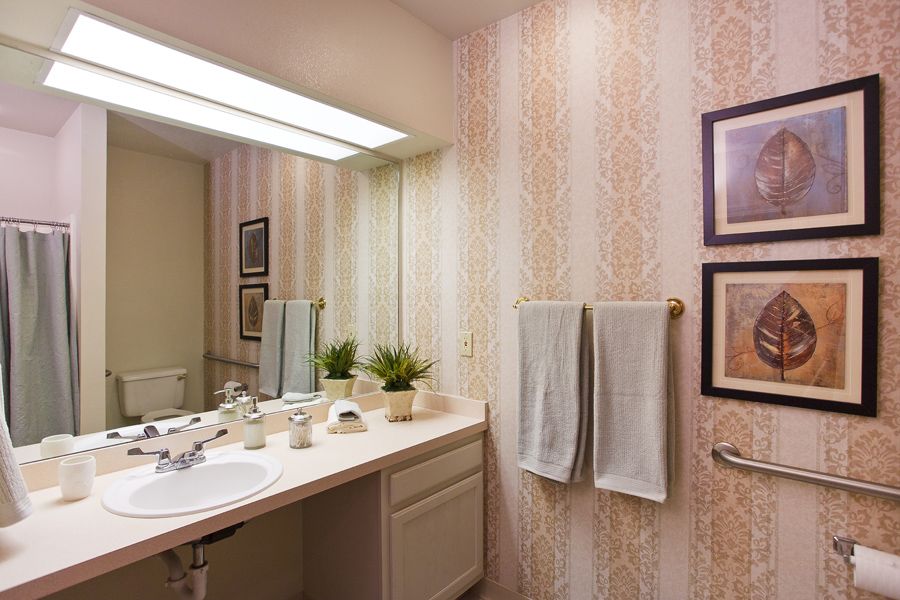 A cozy bathroom with light wallpaper, a mirror, and neatly arranged towels.