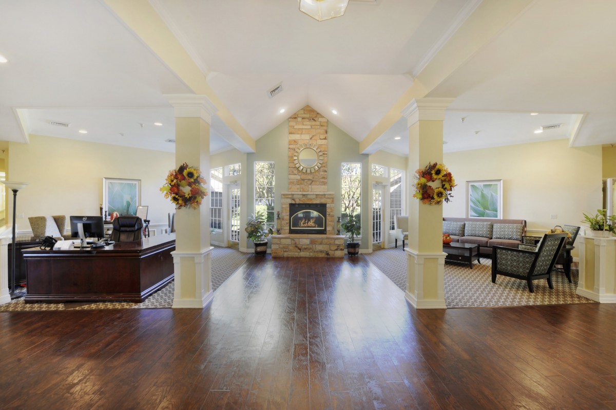 A spacious living room with a central fireplace, featuring hardwood floors, vaulted ceilings, and decorative columns.
