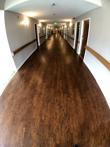 A wide-angle view of a well-lit hallway with wooden flooring and doors on either side.