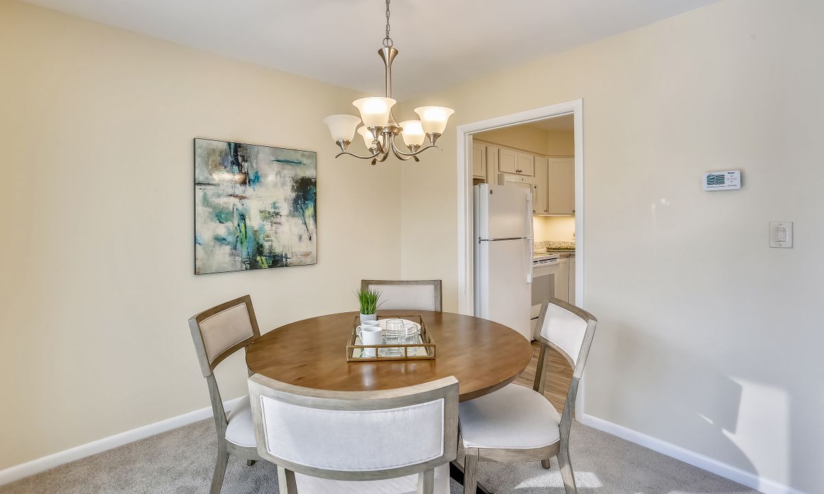 A cozy dining room featuring a round wooden table with chairs, illuminated by an elegant chandelier and adorned with modern wall art.