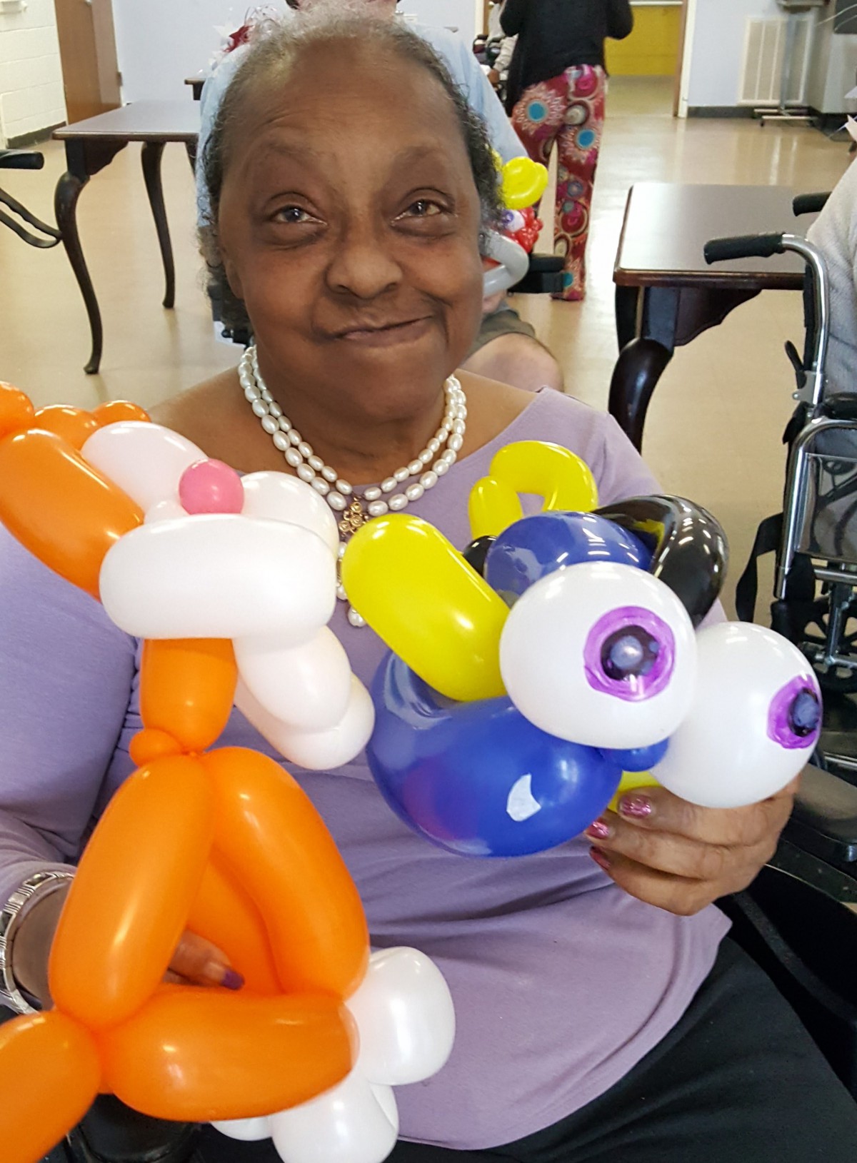 A woman smiling while holding colorful balloon sculptures indoors.