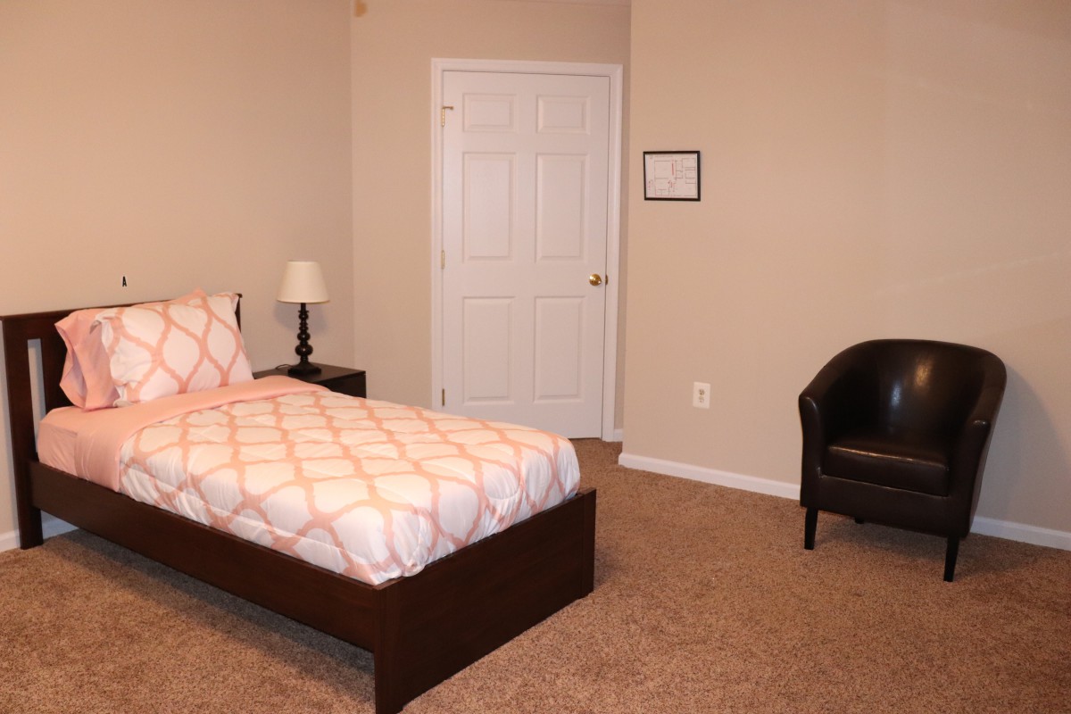 A minimalist bedroom with a single bed, lamp, and chair.