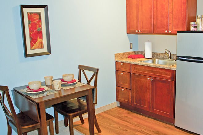 A cozy kitchen and dining area with wooden cabinets, a small table set for two, and wall art.