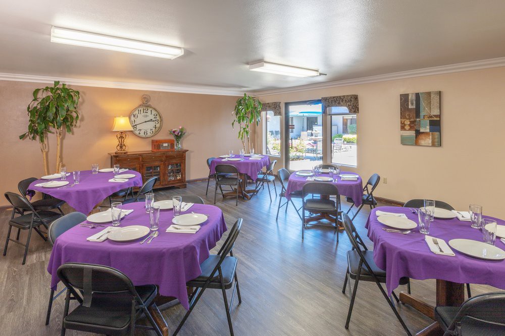 A dining room setup with multiple tables covered in purple tablecloths.