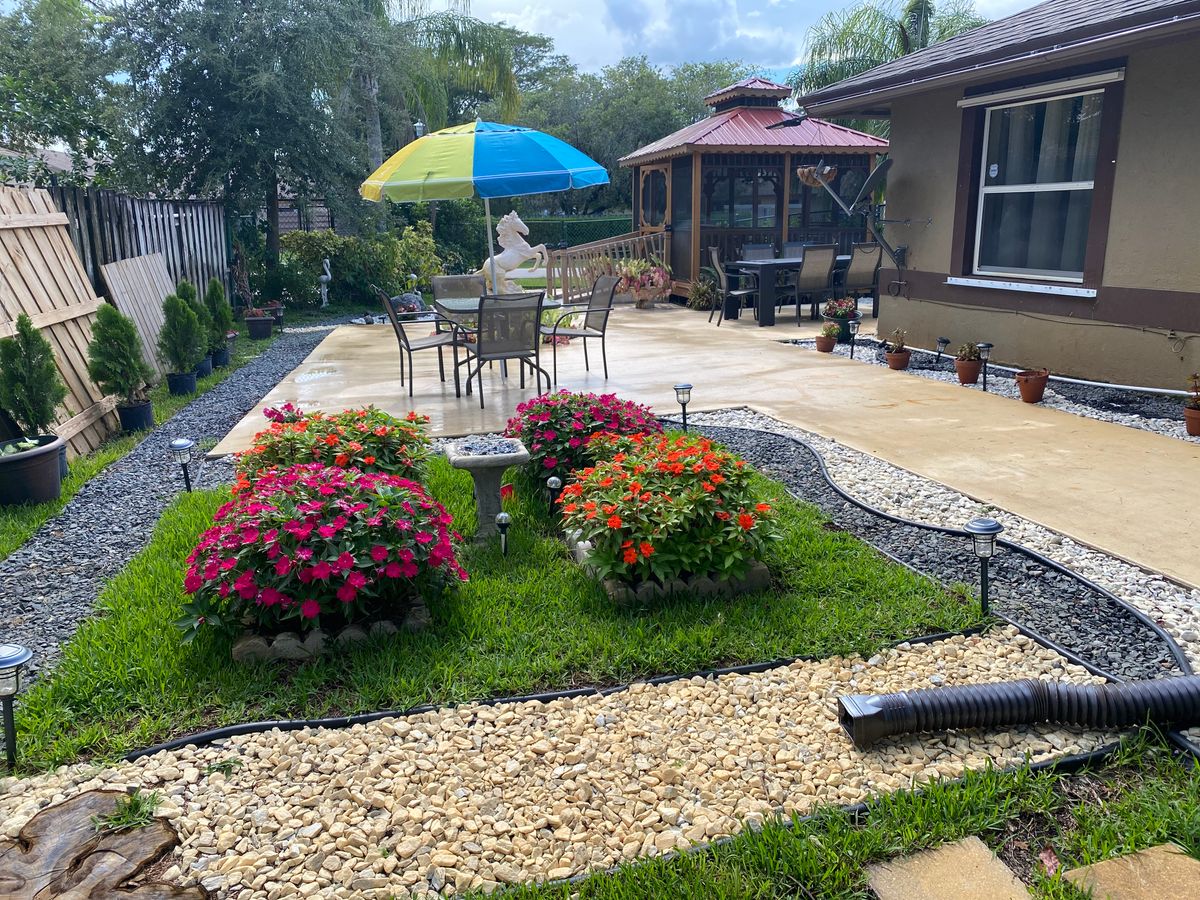 A beautifully landscaped backyard with a patio area, featuring colorful flowers and outdoor seating under an umbrella.