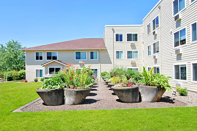 A residential building with a garden featuring large potted plants along a pathway.