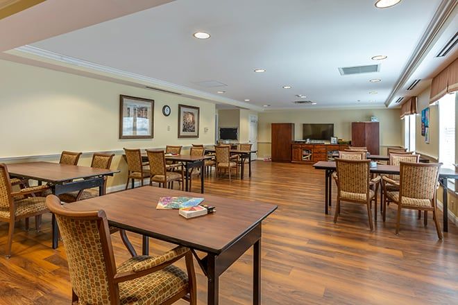 A spacious community dining room with wooden floors and neatly arranged tables and chairs.