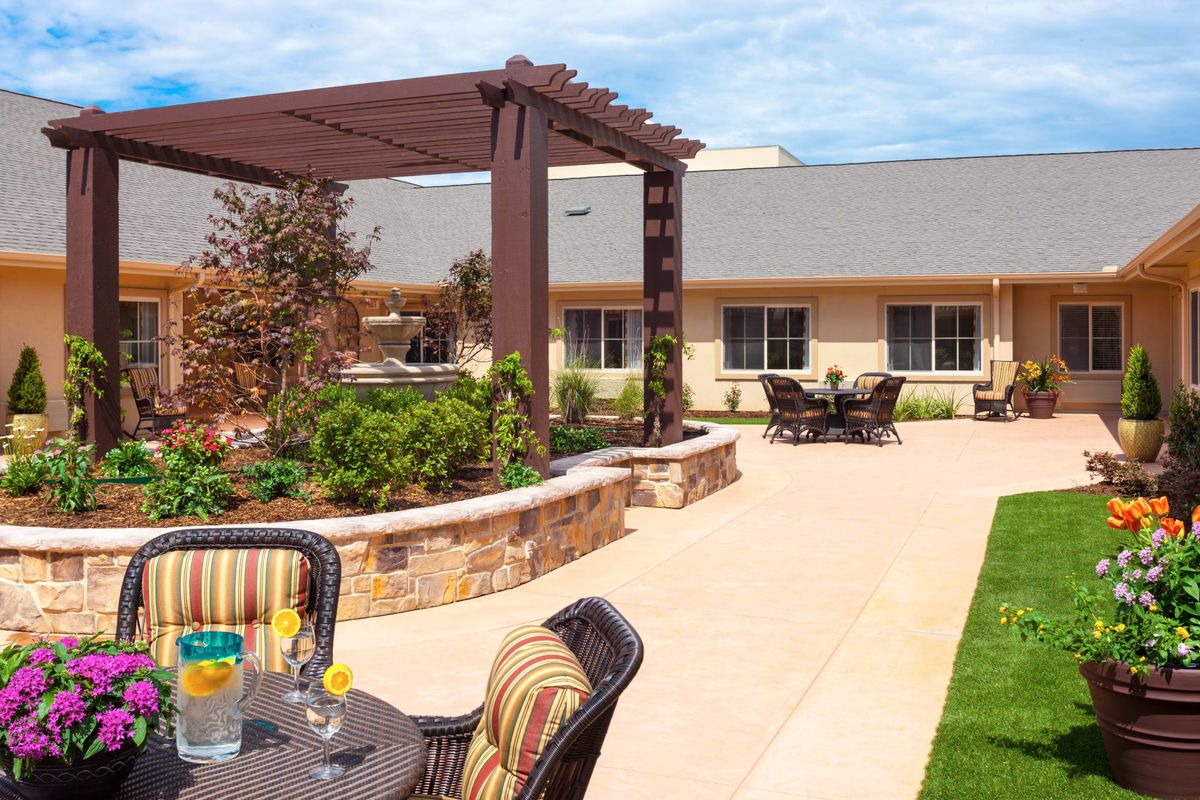 A spacious outdoor patio area featuring a pergola, seating arrangements, and lush garden landscaping.