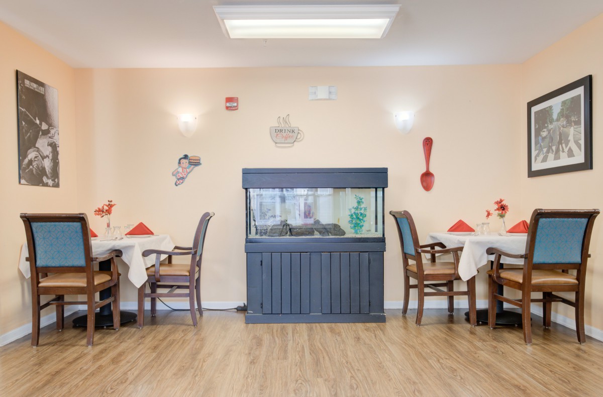 A cozy dining area featuring a central fish tank, surrounded by tables with neatly arranged chairs and decorative wall art.