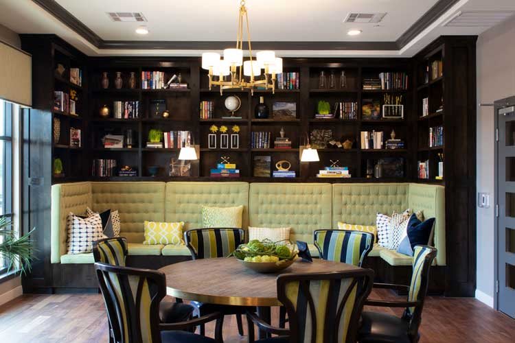 A modern living room with a cozy seating area, bookshelves, and a central round table under a decorative chandelier.