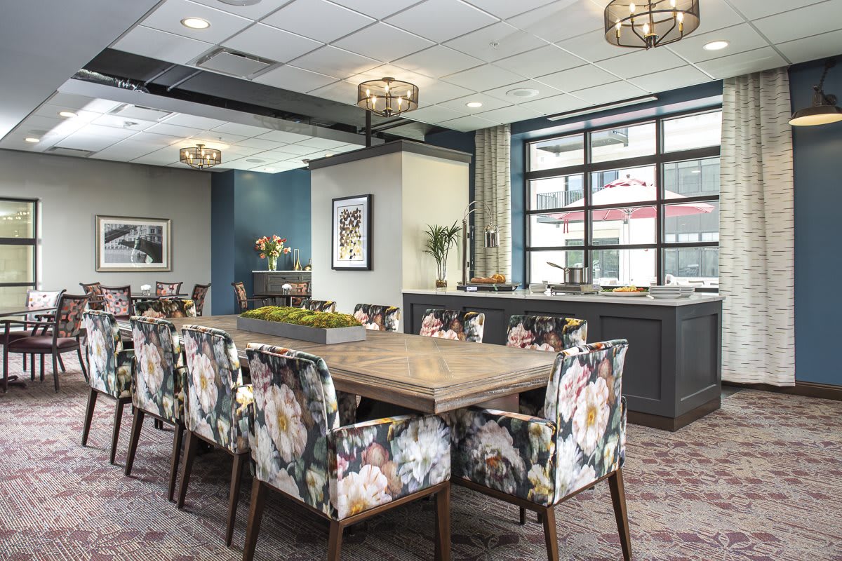 A modern dining room with floral upholstered chairs and a large wooden table, illuminated by stylish chandeliers.