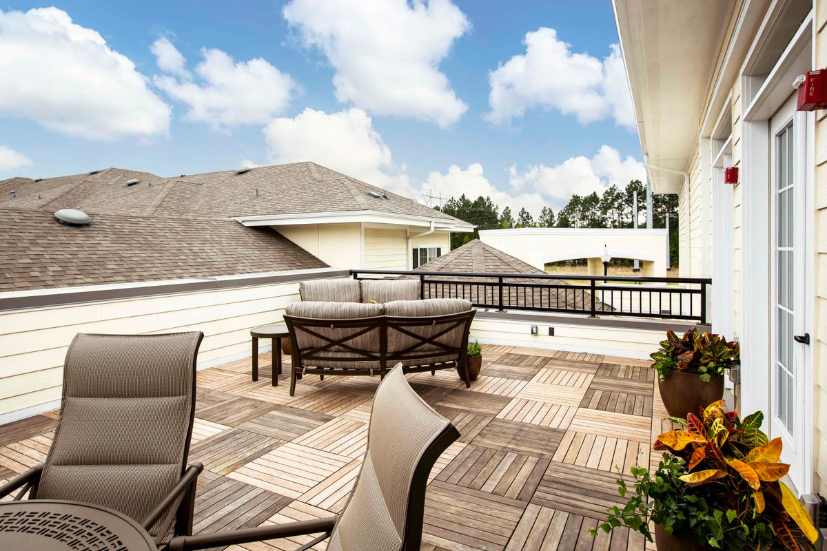 A spacious rooftop patio featuring comfortable outdoor furniture and wooden decking under a partly cloudy sky.