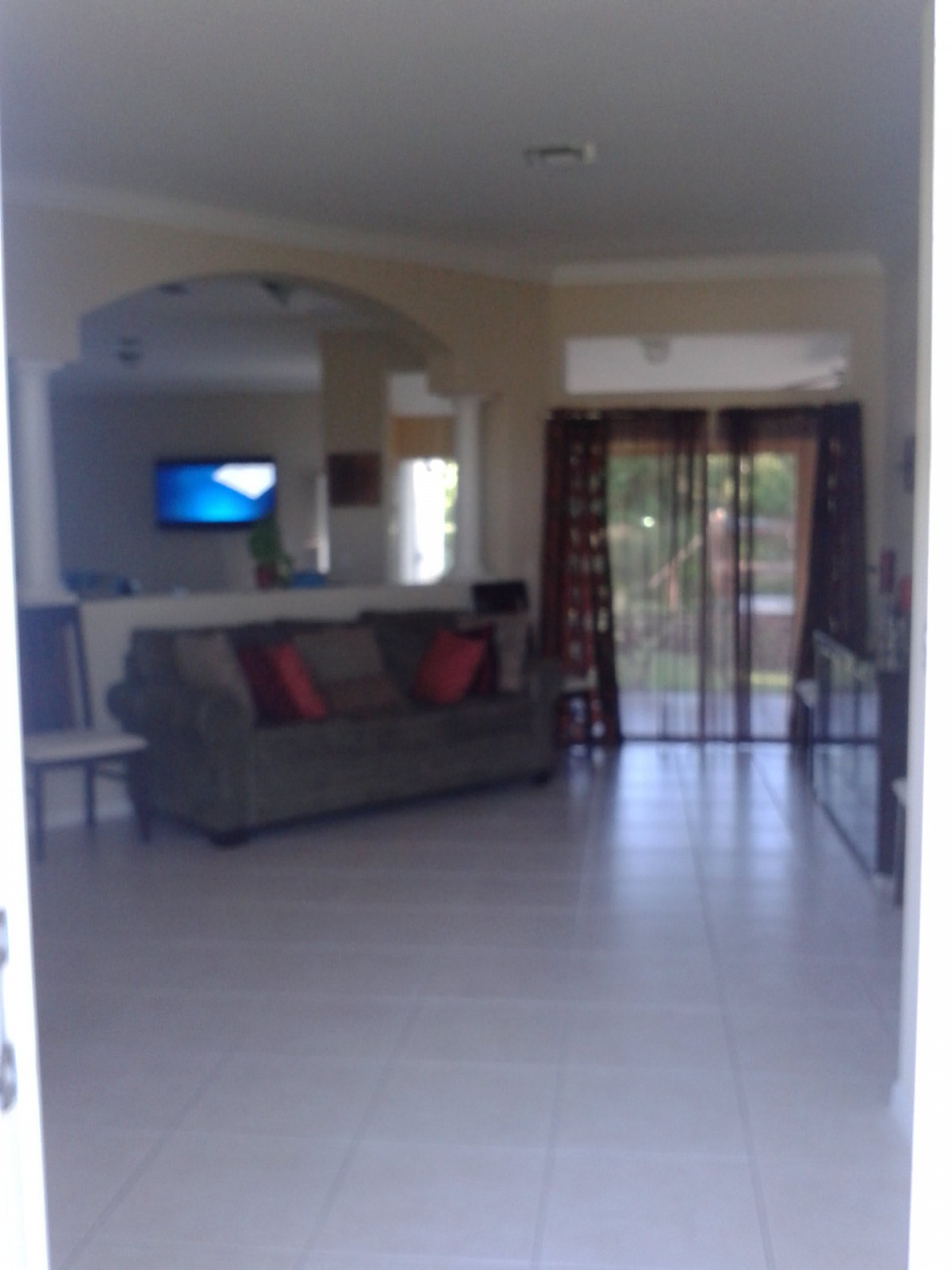 A spacious living room with a sofa, television, and large windows.