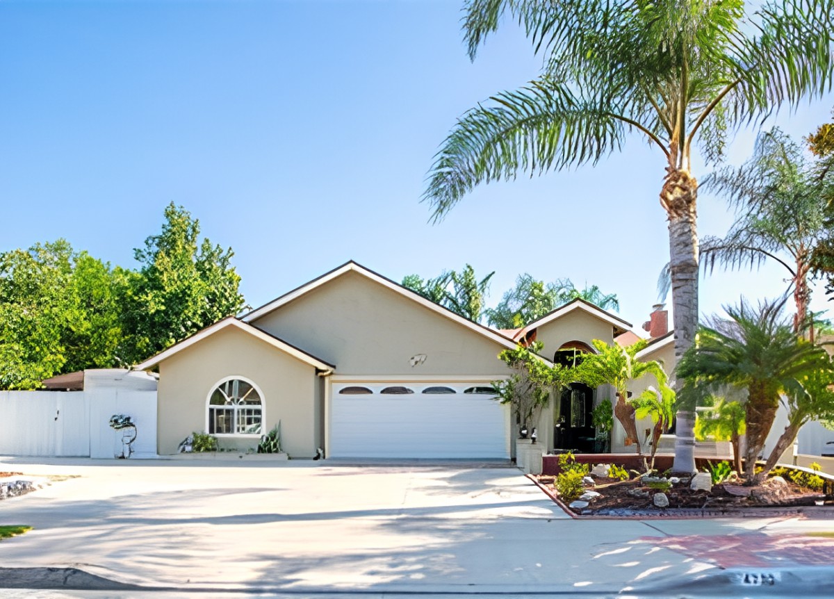 A suburban house with a two-car garage and palm trees in the front yard.