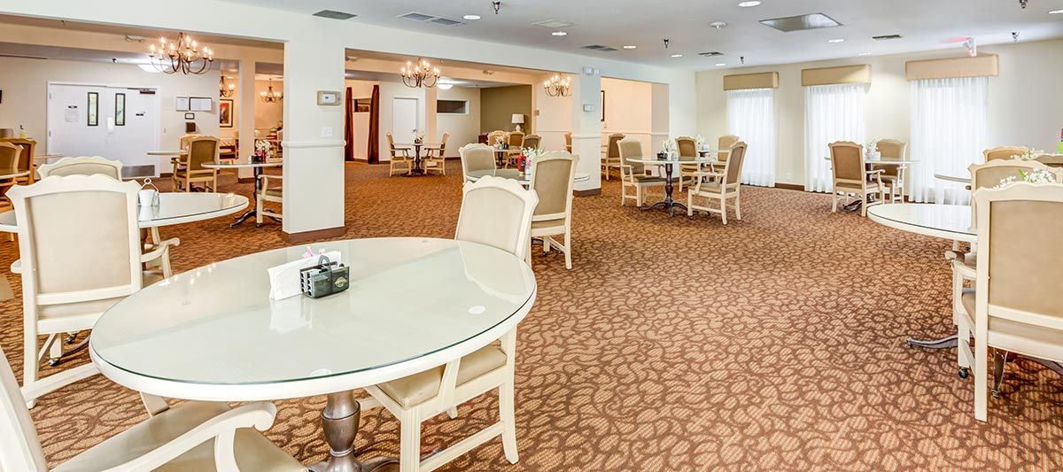 A spacious dining area with several tables and chairs, featuring a carpeted floor and soft lighting.