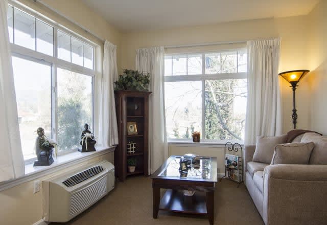 A cozy living room with large windows allowing natural light to fill the space, featuring a comfortable couch and a wooden coffee table.
