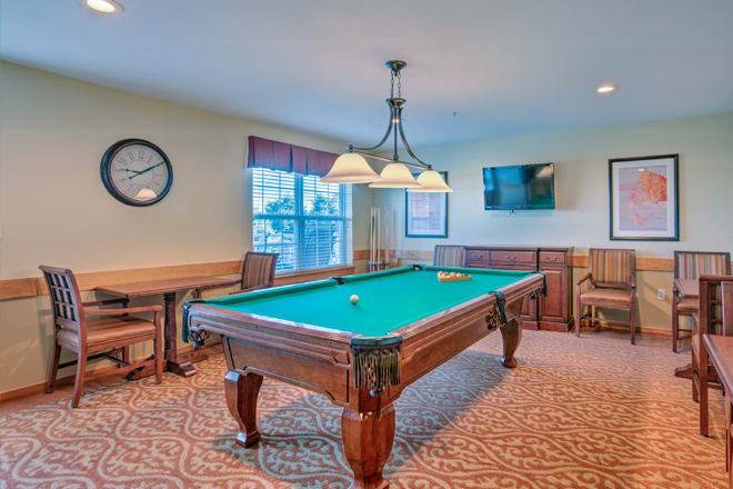 A cozy game room featuring a billiards table under a light fixture, with a television mounted on the wall.