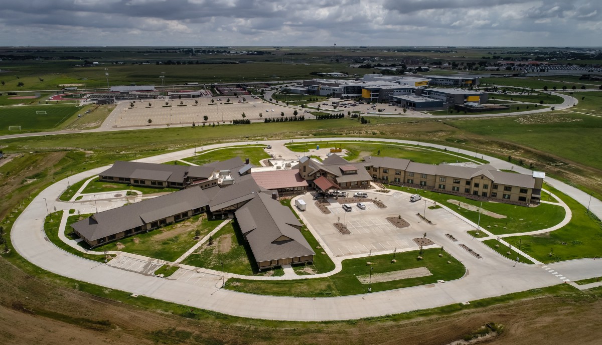An aerial view of a large building complex with surrounding parking areas and green spaces under a cloudy sky.