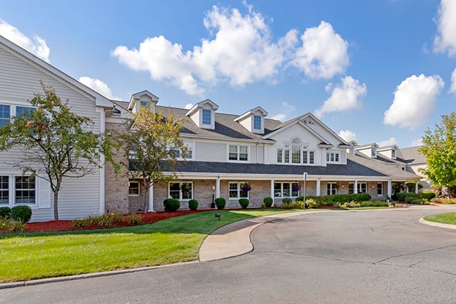 A large residential building with a well-maintained front yard under a partly cloudy sky.