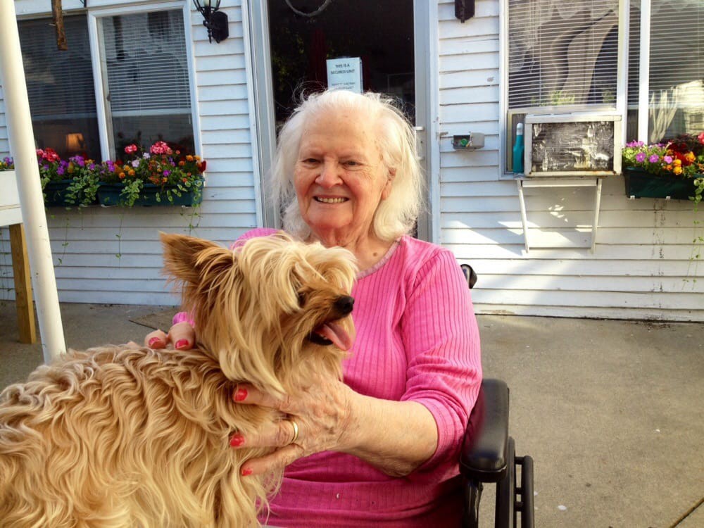 An elderly woman smiling while holding her dog outside.