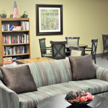 A cozy living room with a striped sofa, a well-stocked bookshelf, and a seating area with chairs around a table.
