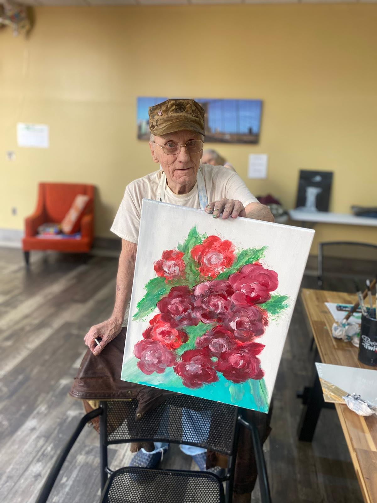 A person proudly displays a vibrant floral painting in an art studio.