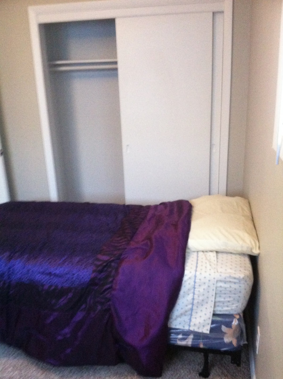 A small bedroom with a single bed covered in a purple blanket.