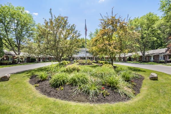 A beautifully landscaped garden with trees and shrubs surrounding a flagpole, adjacent to a driveway.