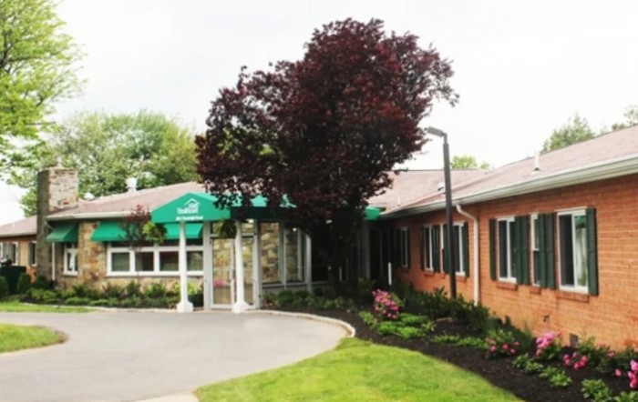 A building entrance with a green awning and surrounding trees and landscaping.
