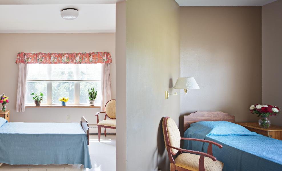 A cozy interior with a bedroom and living area, featuring chairs, tables, and natural light from a window.