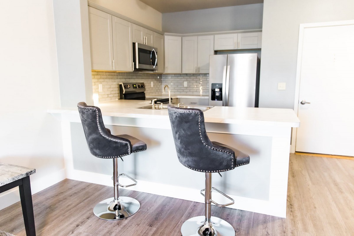 A modern kitchen with white cabinets and stainless steel appliances, featuring a countertop with two bar stools.