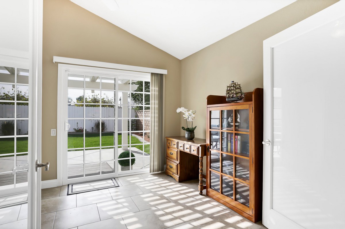 A bright room with a wooden desk and cabinet, featuring large glass doors that open to a garden.