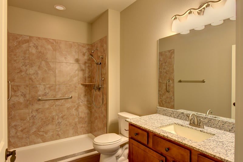 A clean and modern bathroom with a tiled shower, vanity, and large mirror.