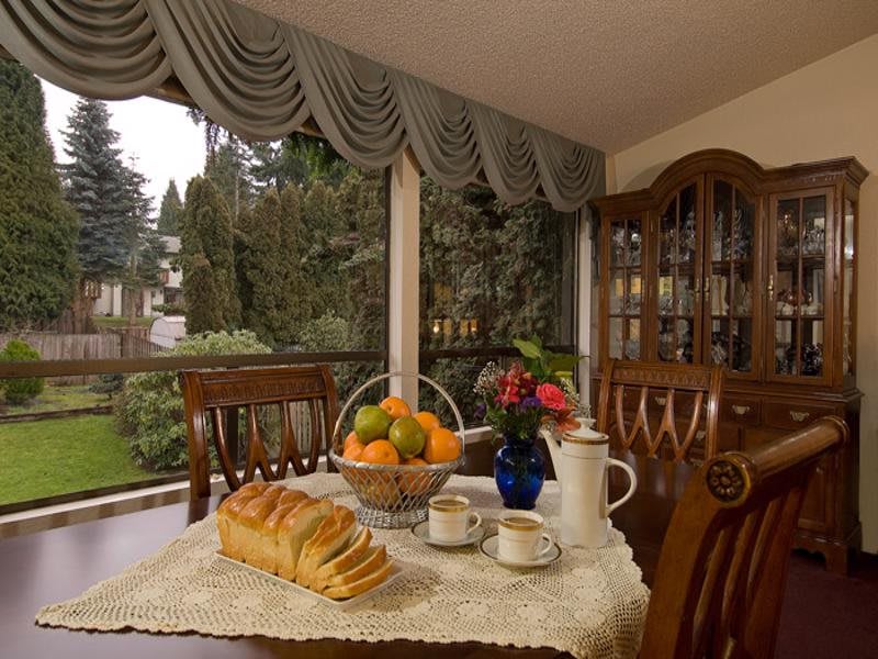 A cozy dining room scene with a table set for tea, featuring freshly sliced bread, a fruit basket, and a vase of flowers.
