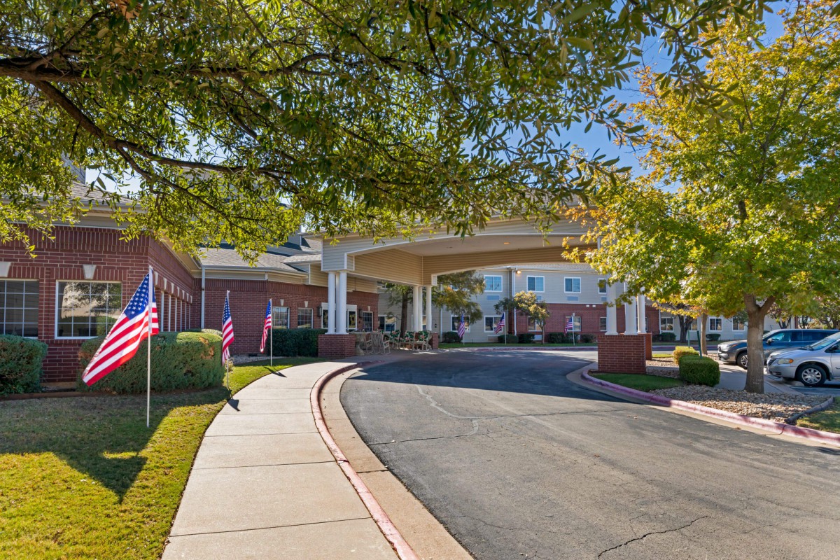 A welcoming entrance to a building with a curved driveway and flags lining the walkway under a sunny sky.