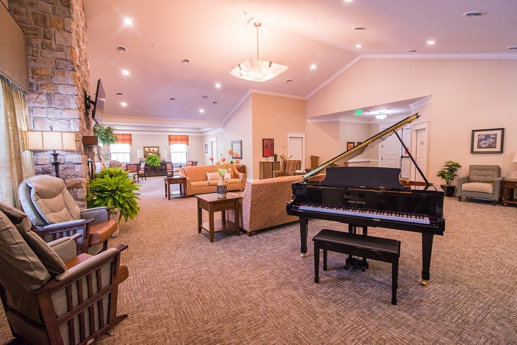 A spacious and elegantly furnished living room featuring a grand piano, comfortable seating, and warm lighting.