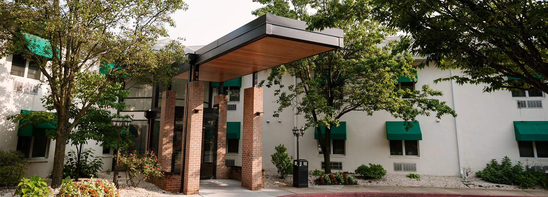 A building entrance with a wooden canopy surrounded by trees.