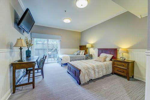 A cozy bedroom with two beds, a desk, and a TV mounted on the wall.